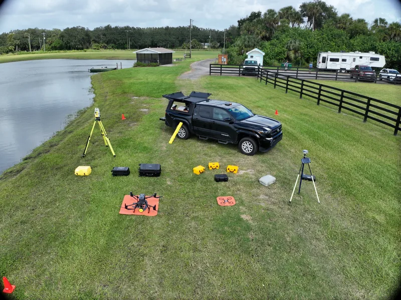 Aerial view of a SurveyFy truck with LiDAR drone, GNSS receivers and total station set up beside a lake
