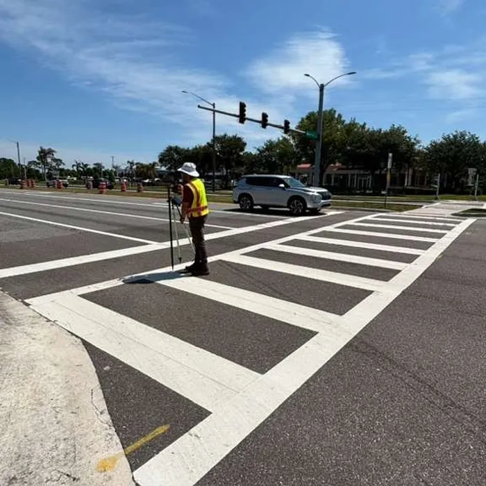Surveyor with a GNSS rover locating a point on a street crosswalk in Florida